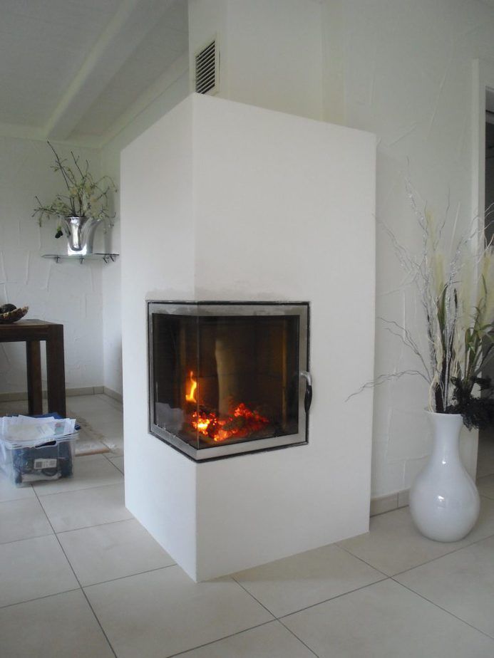 Modernes weißes Wohnzimmer mit einem zentralen Kamin aus Glasfront, in dem ein Feuer brennt.