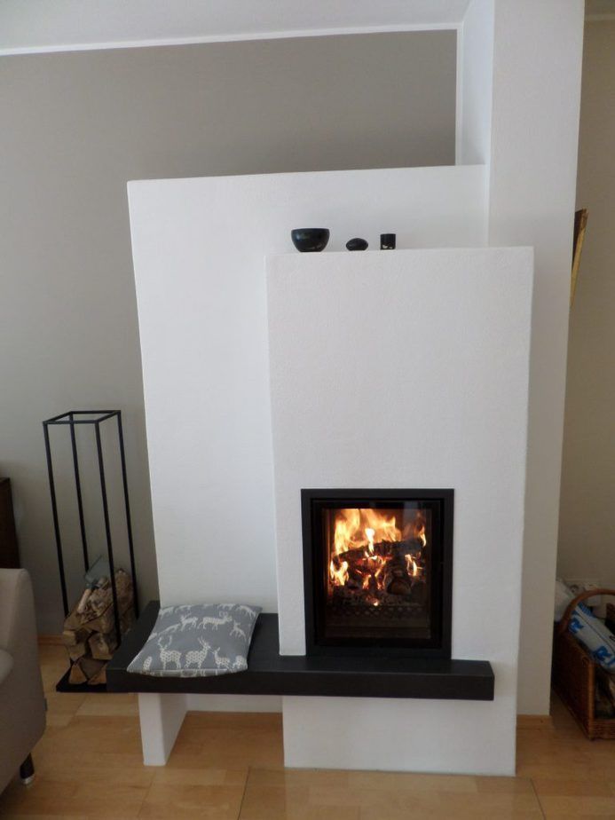 Moderner weißer Kamin mit brennendem Feuer, schwarzer Kaminplatte und Sitzbank in einem Wohnzimmer.