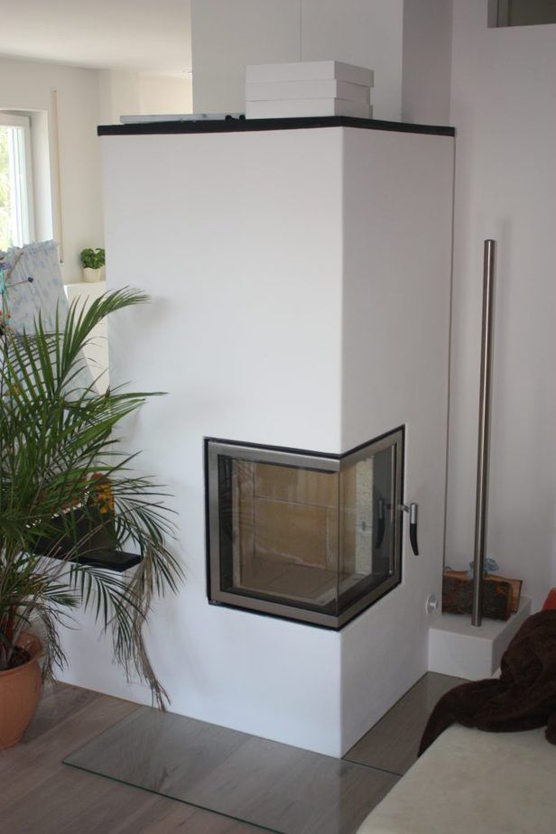 Moderner weißer Kamin mit Glastüren in einem hellen Wohnzimmer, neben einer Topfpalme.