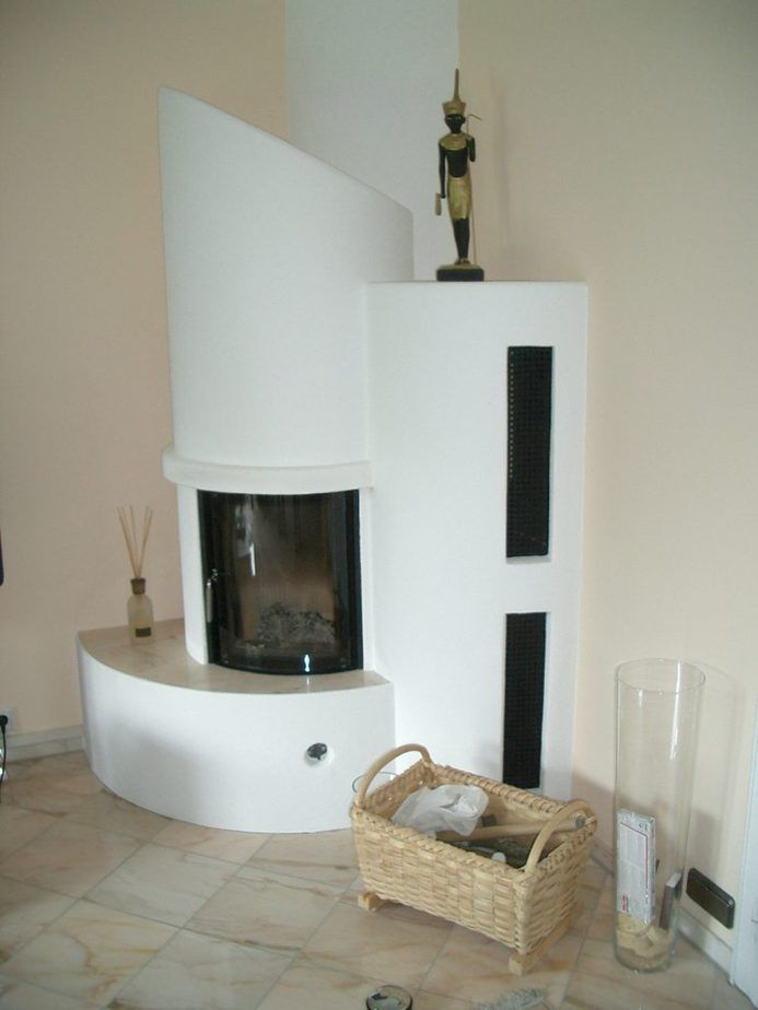 Ein weißer, geschwungener Kamin in einem minimalistischen Wohnzimmer mit einem Korb und Glasvasen.