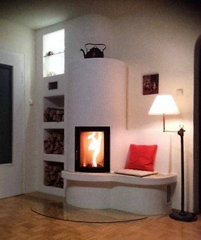 Gemütliche Wohnzimmerecke mit weißem Kamin, rotem Kissen, Stehlampe und kleiner Regalnische.