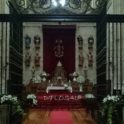 Altar con acentos rojos, arreglos florales y estatuas religiosas.