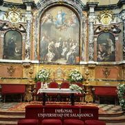 Interior de la Universidad de Salamanca, adornado con pinturas, una mesa decorada y arreglos florales.