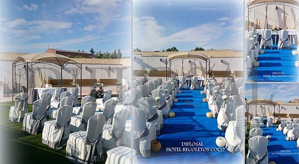 Montaje de evento al aire libre con sillas blancas, alfombra azul, bajo un cielo soleado.