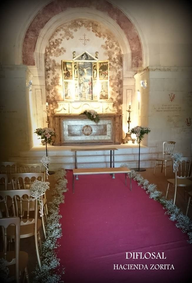Espacio para ceremonias con pasillo y altar con alfombra roja. Flores blancas adornan el pasillo.