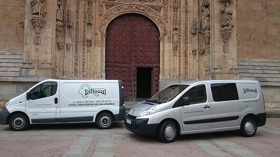 Dos furgonetas de reparto estacionadas frente a la entrada de una iglesia. Una blanca y la otra plateada.
