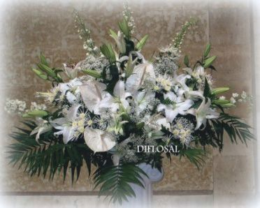 Arreglo floral blanco en jarrón blanco. Incluye lirios, anturios y follaje.