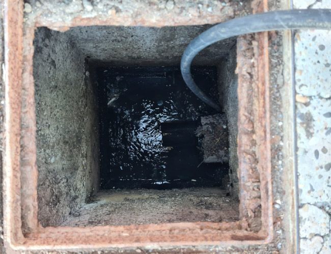 Una tapa de alcantarilla por la que sale agua y de la que sale una manguera.