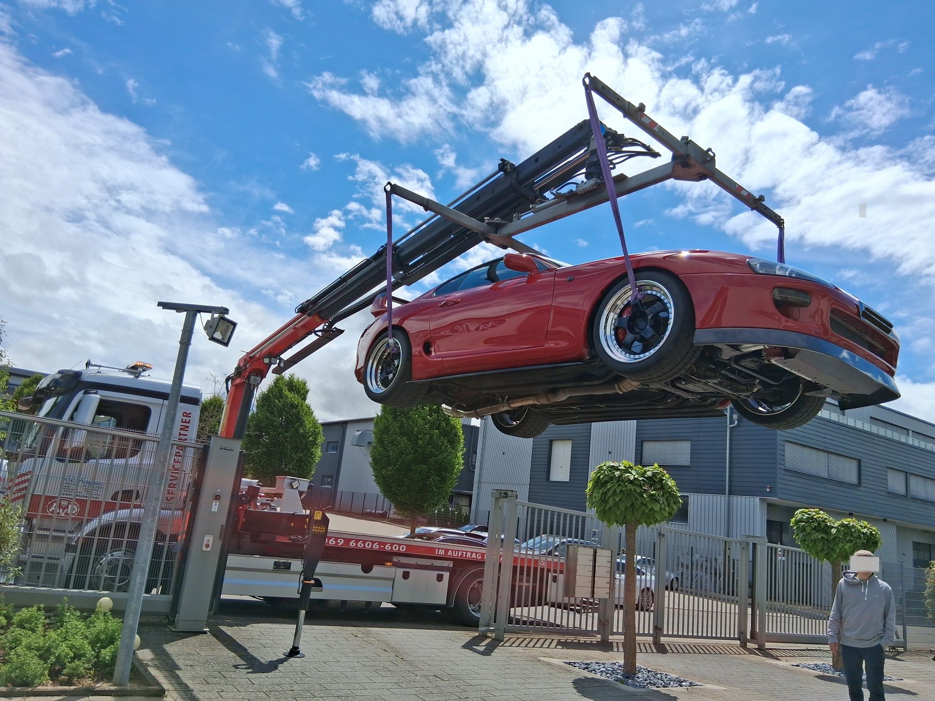 Ein roter Sportwagen wird von einem Kran angehoben.