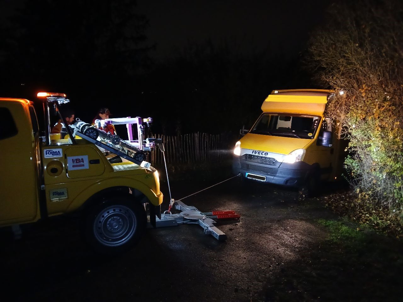 Ein gelber Abschleppwagen schleppt nachts einen gelben Lieferwagen ab.