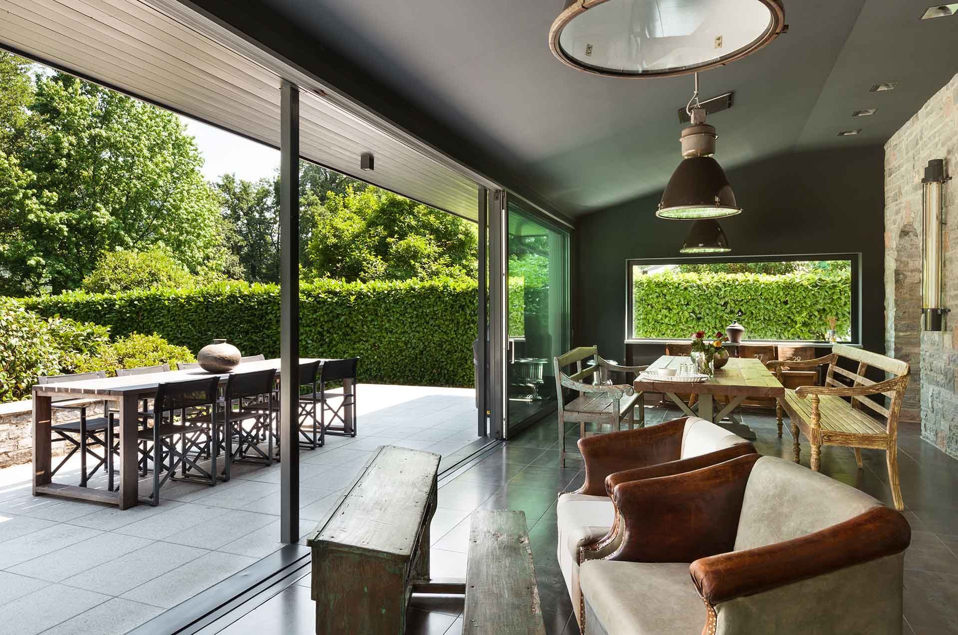 Salon moderne avec portes vitrées ouvertes donnant sur un patio, comprenant des canapés aux tons neutres et une table à manger.