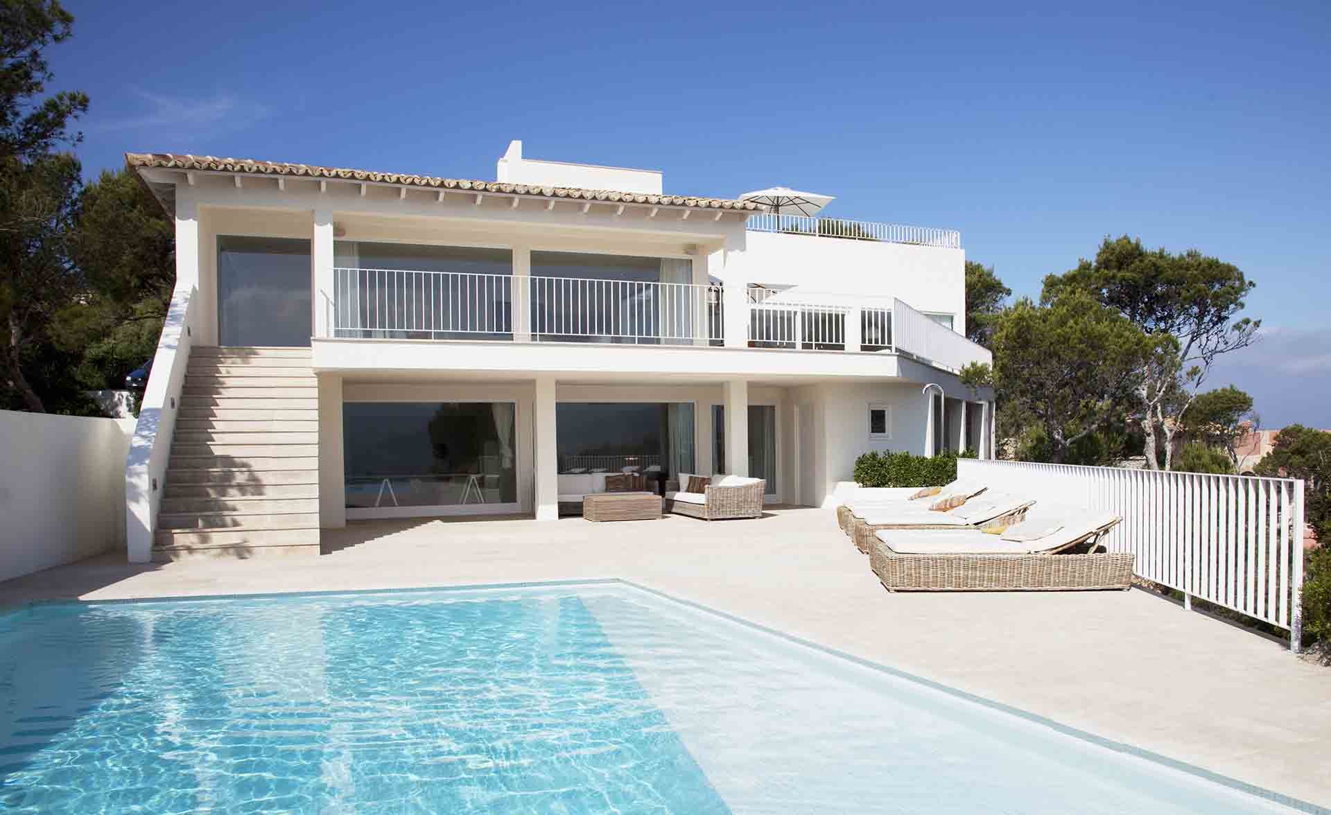 Villa blanche moderne avec piscine, chaises longues et vue sur l'océan sous un ciel bleu azur.