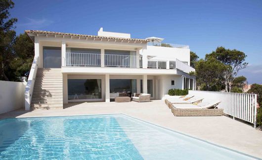 Villa blanche moderne avec piscine et chaises longues sous un ciel bleu azur.