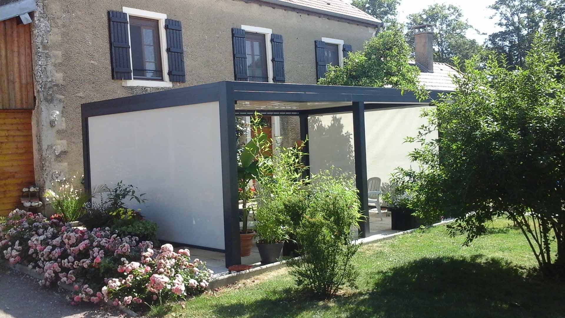 Patio de jardin aux murs blancs et à l'encadrement sombre, jouxtant une maison en briques, entouré de fleurs et de verdure.