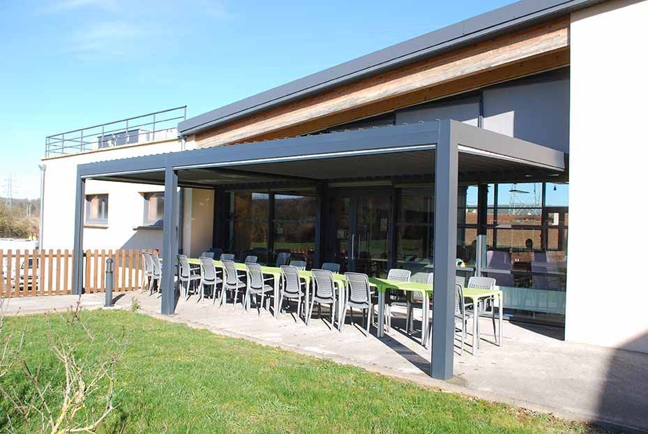 Bâtiment blanc moderne avec terrasse couverte, tables et chaises d'extérieur et premier plan gazonné