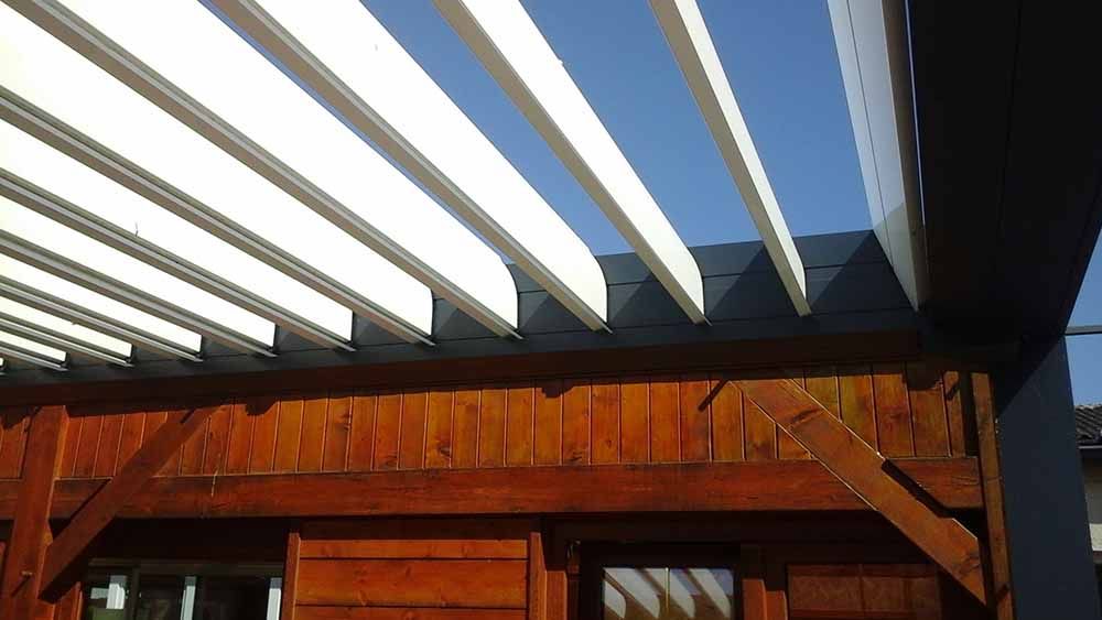 Bâtiment en bois sous une pergola aux poutres blanches se détachant sur un ciel bleu.