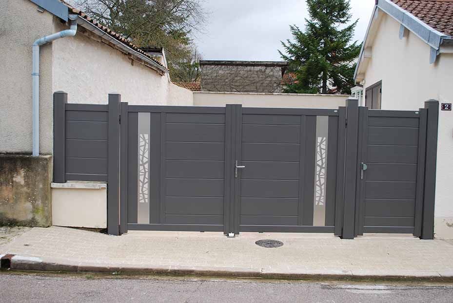 Portail d'allée en métal gris entre deux maisons dans une rue résidentielle.