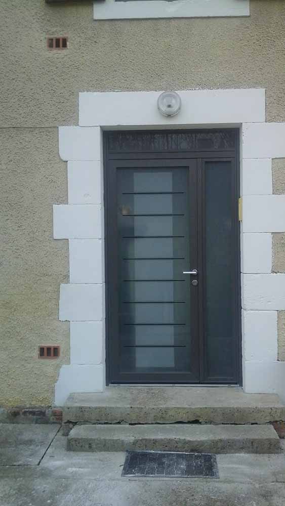 Porte d'entrée gris foncé avec panneaux de verre dépoli, encadrée de moulures blanches sur une façade en pierre.