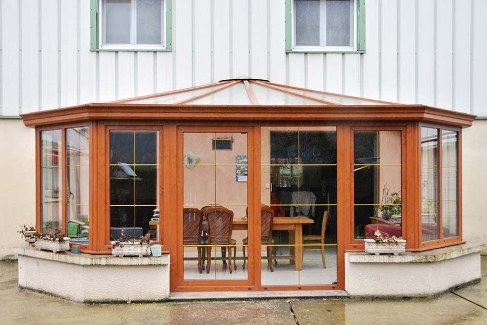 Véranda à ossature en bois avec portes et fenêtres vitrées, attenante à une maison blanche