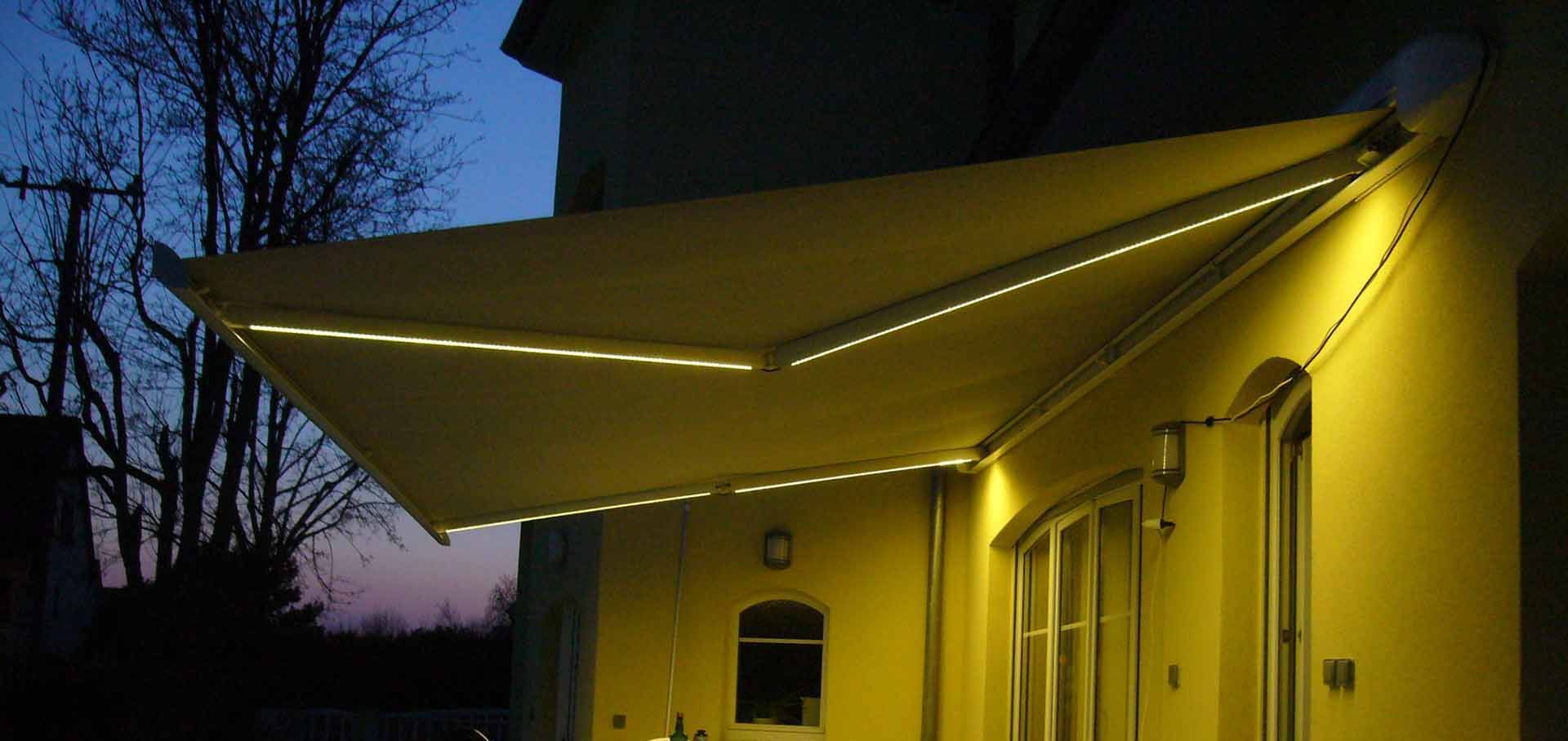 Auvent jaune au-dessus de l'entrée d'un bâtiment au crépuscule, éclairé par des lumières extérieures