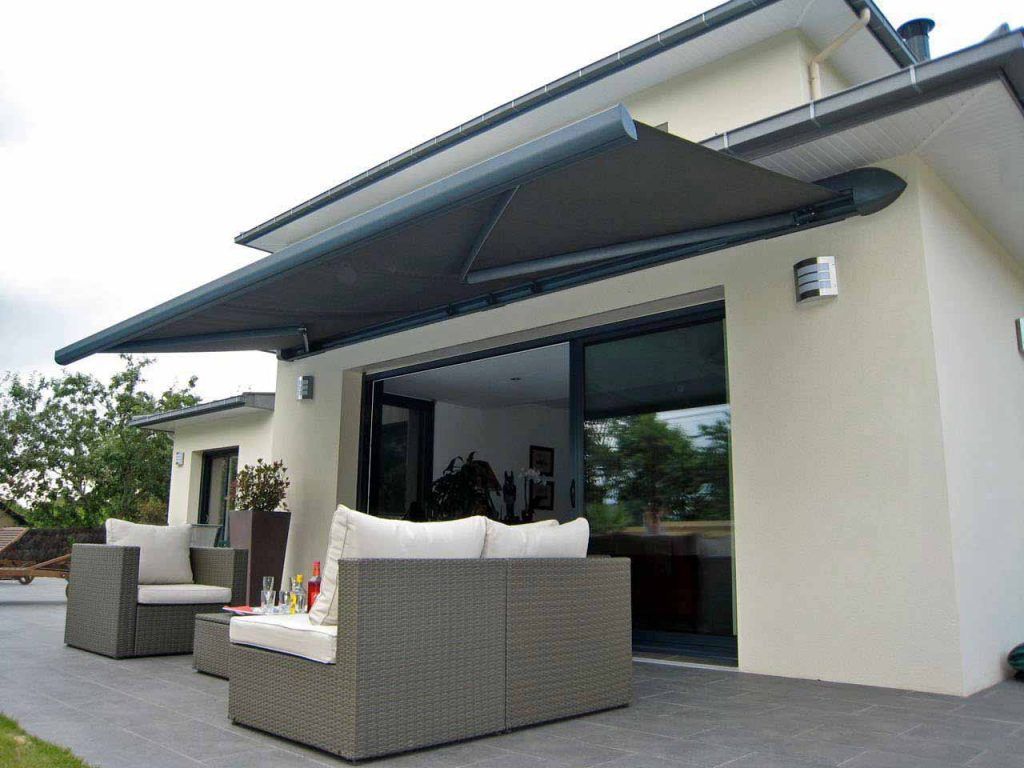 Terrasse moderne avec sièges en osier gris et un grand auvent rétractable à l'extérieur d'une maison
