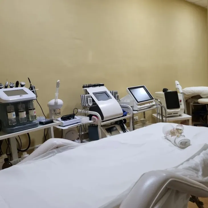 Sala de spa con varias máquinas de tratamientos faciales y camilla de masaje. Paredes beige.