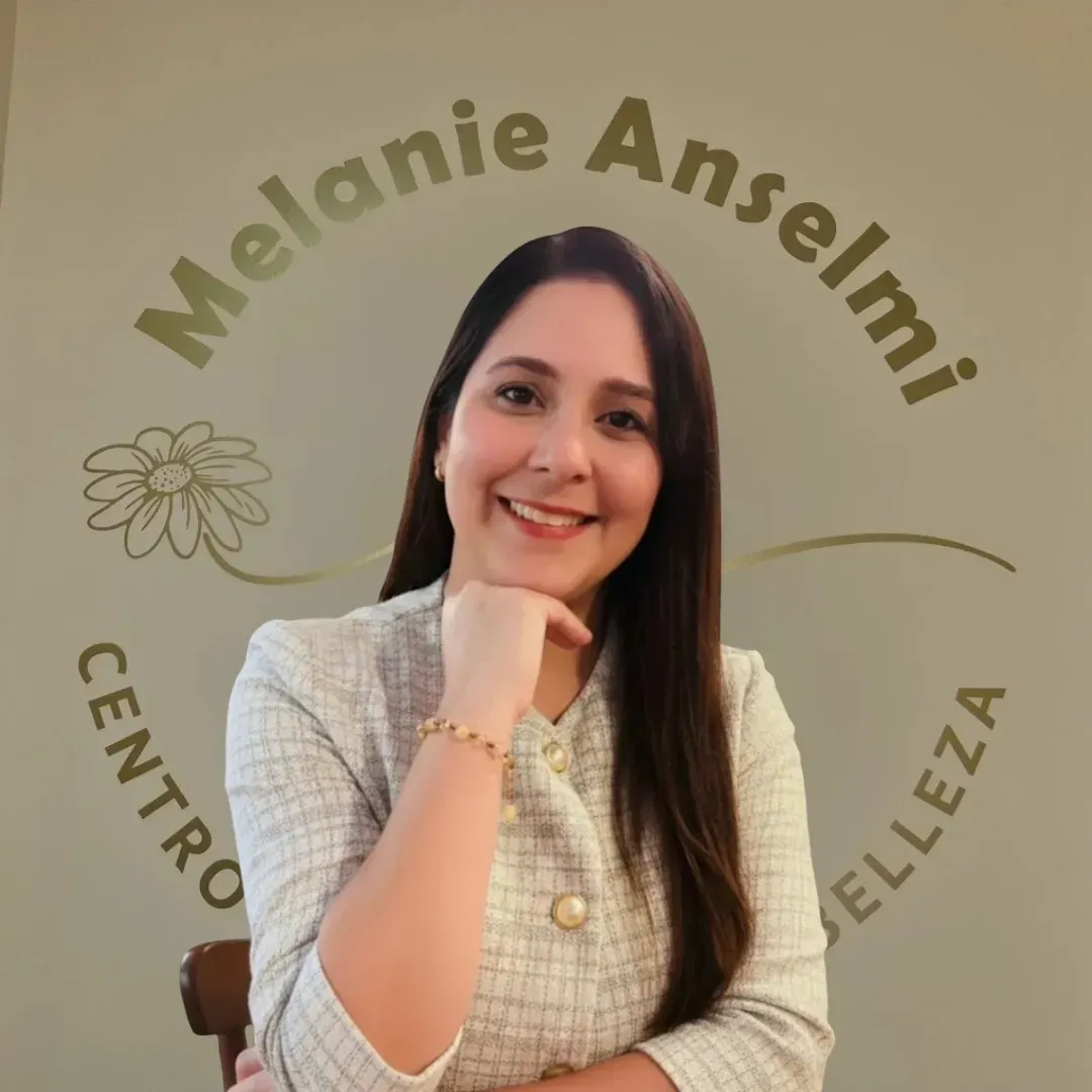 Mujer sonriendo, con la mano en la barbilla, frente a un cartel que dice 