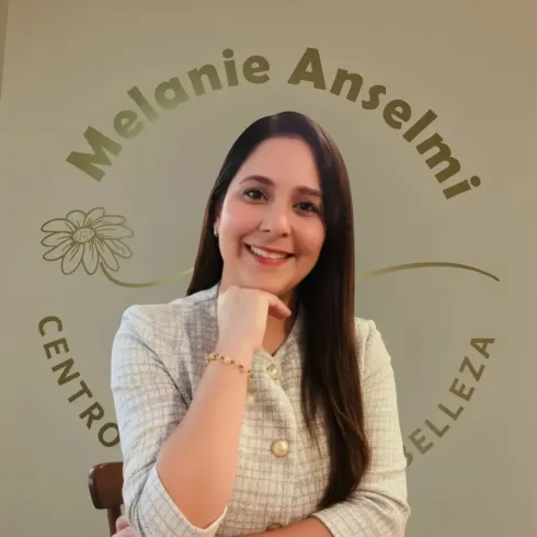 Mujer sonriendo, con la mano en la barbilla, frente a un cartel que dice 