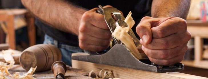 Un hombre está usando un cepillo para cepillar un trozo de madera.