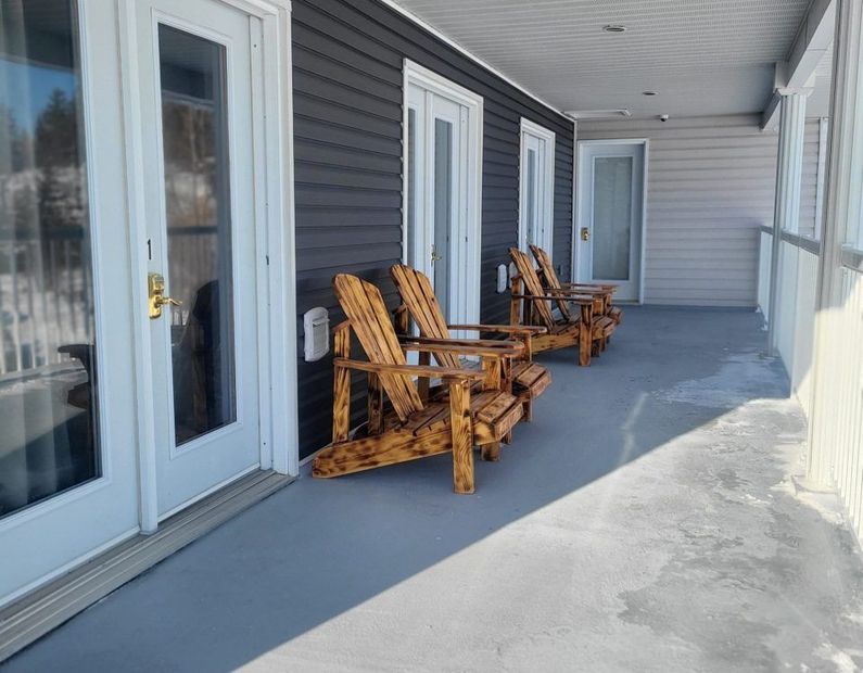 Covered patio with wooden rocking chairs along sliding glass doors and white siding