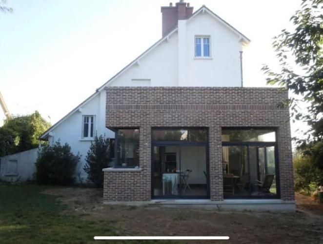 Maison en briques avec une véranda vitrée et une façade supérieure blanche, vue depuis le jardin au crépuscule