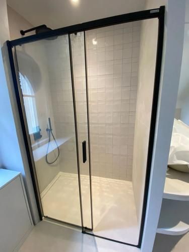 Cabine de douche vitrée à cadre noir, murs carrelés de blanc et receveur beige dans une salle de bains moderne
