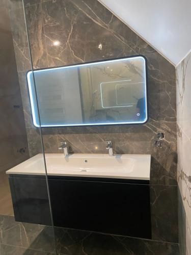 Meuble-lavabo moderne avec miroir éclairé, vasque blanche et meuble foncé, contre des murs carrelés de marbre