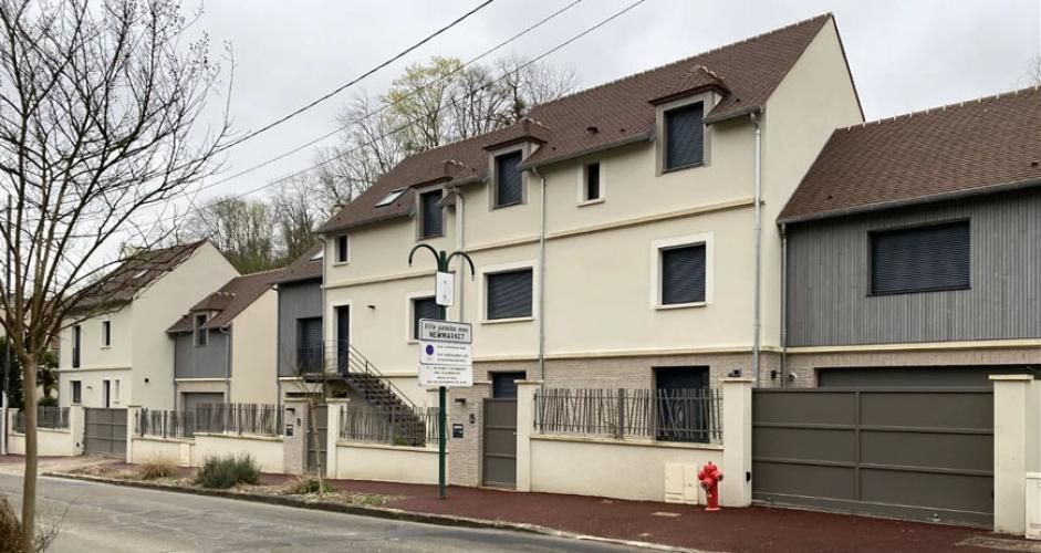 Rangée de maisons couleur crème dans une rue calme bordée d’arbres dénudés, avec une grande porte de garage