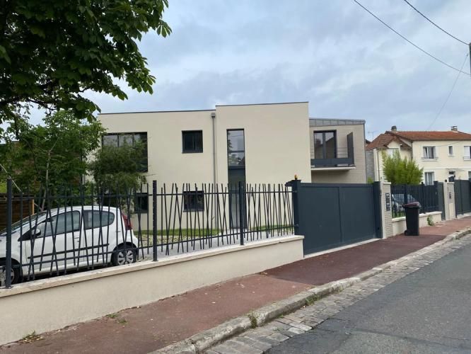 Maison moderne beige derrière une clôture noire.