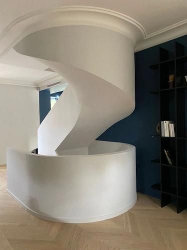 Escalier en colimaçon moderne blanc dans une pièce lumineuse avec un parquet clair et une bibliothèque intégrée sombre.