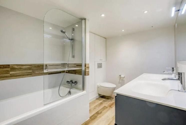 Salle de bains moderne blanche avec baignoire, paroi de douche en verre, toilettes et meuble double vasque