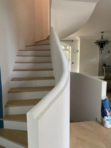 Escalier courbe avec des marches en bois et une rampe blanche dans un intérieur lumineux