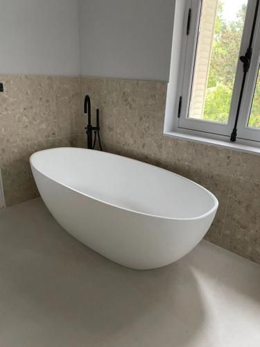 Baignoire ovale blanche moderne et autoportante, près d’une fenêtre dans une salle de bains carrelée