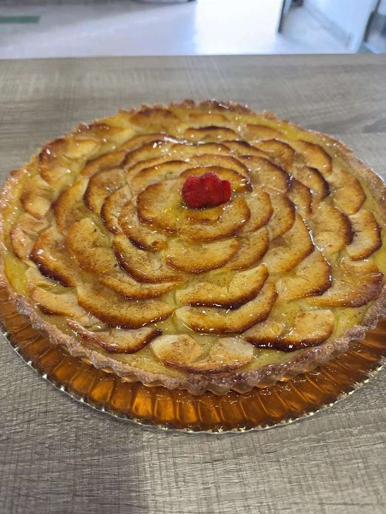 Tarta de manzana con centro de frutos rojos en un molde de vidrio estriado, sobre un mantel gris.