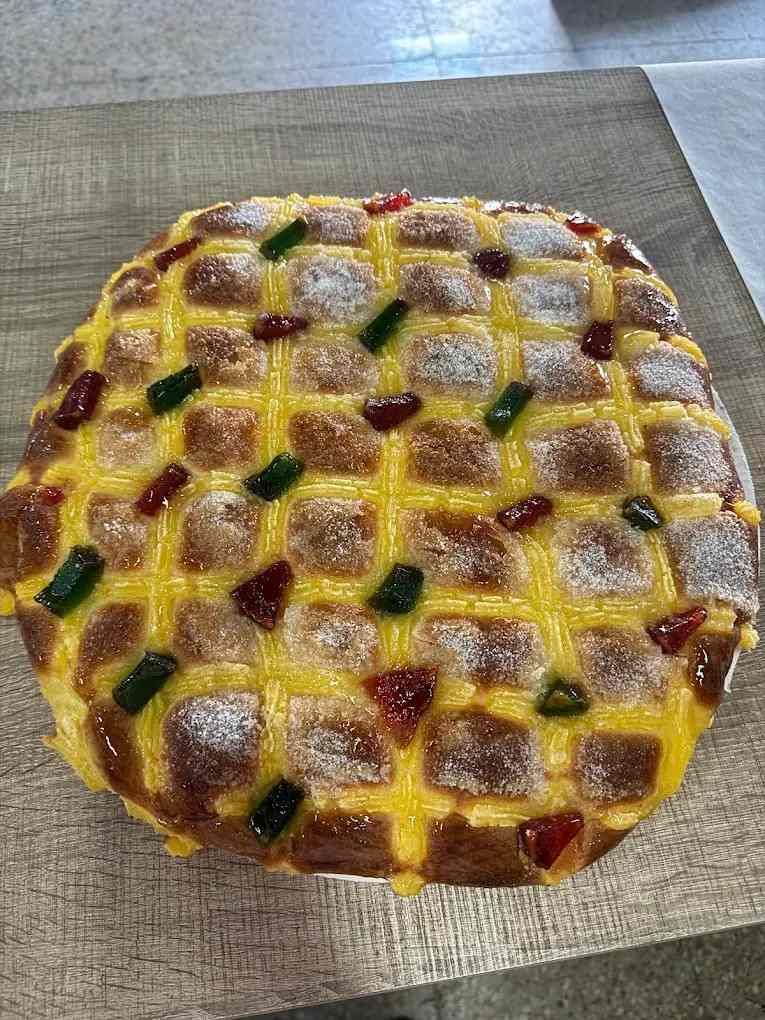 Pastel redondo glaseado cubierto con coloridas frutas confitadas sobre papel pergamino.