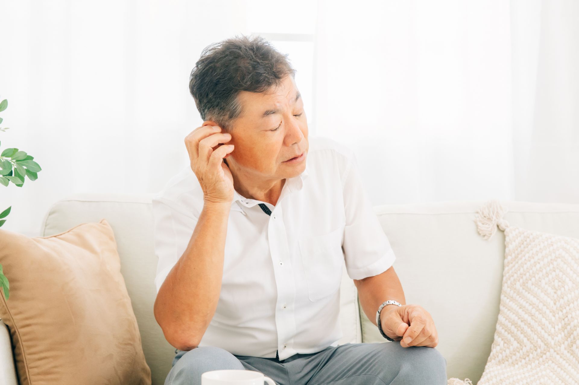 Ein älterer Mann sitzt auf einem Sofa und telefoniert mit einem Mobiltelefon.