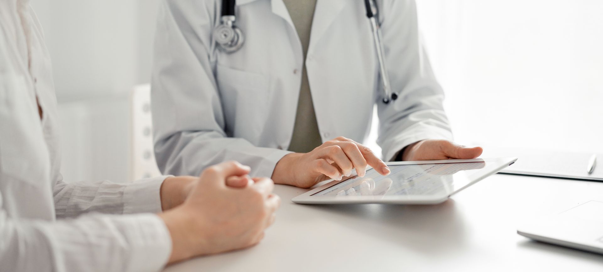 Ein Arzt und ein Patient sitzen an einem Tisch und schauen auf ein Tablet.
