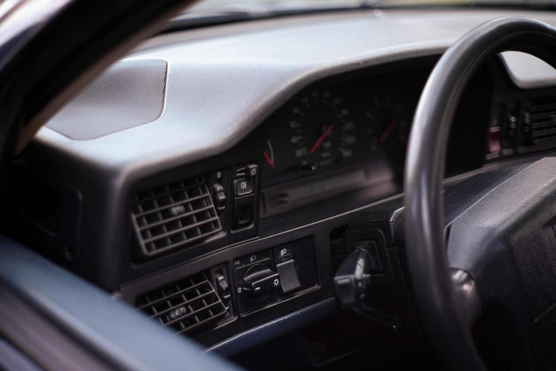 Primer plano del salpicadero gris oscuro de un coche clásico, con indicadores analógicos, salidas de aire y volante.