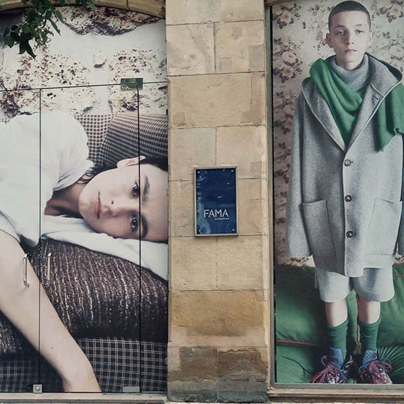 Fachada con dos carteles de moda junto a una pared de azulejos y una placa azul de FAMA.