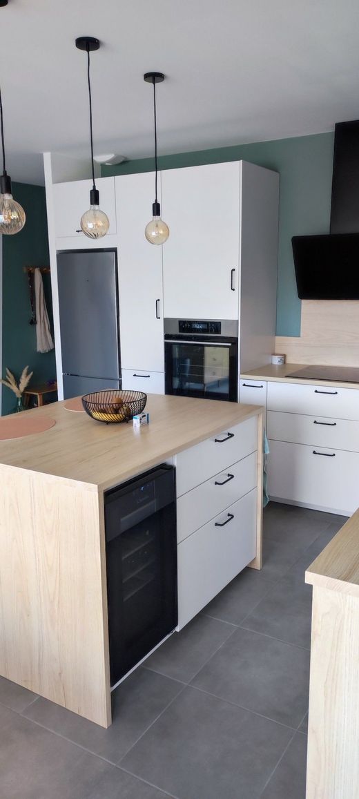 Cuisine moderne avec armoires blanches, îlot en bois et électroménagers noirs.