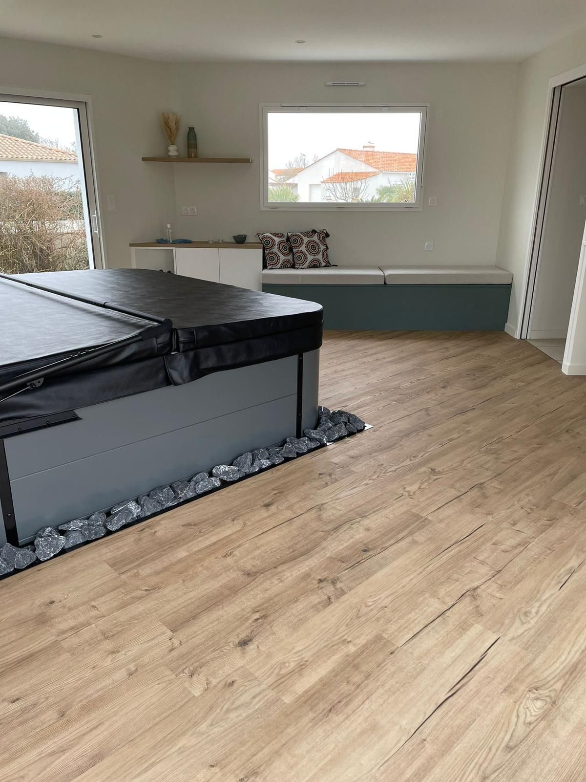 Pièce intérieure avec jacuzzi couvert, sol imitation bois et banquette intégrée.