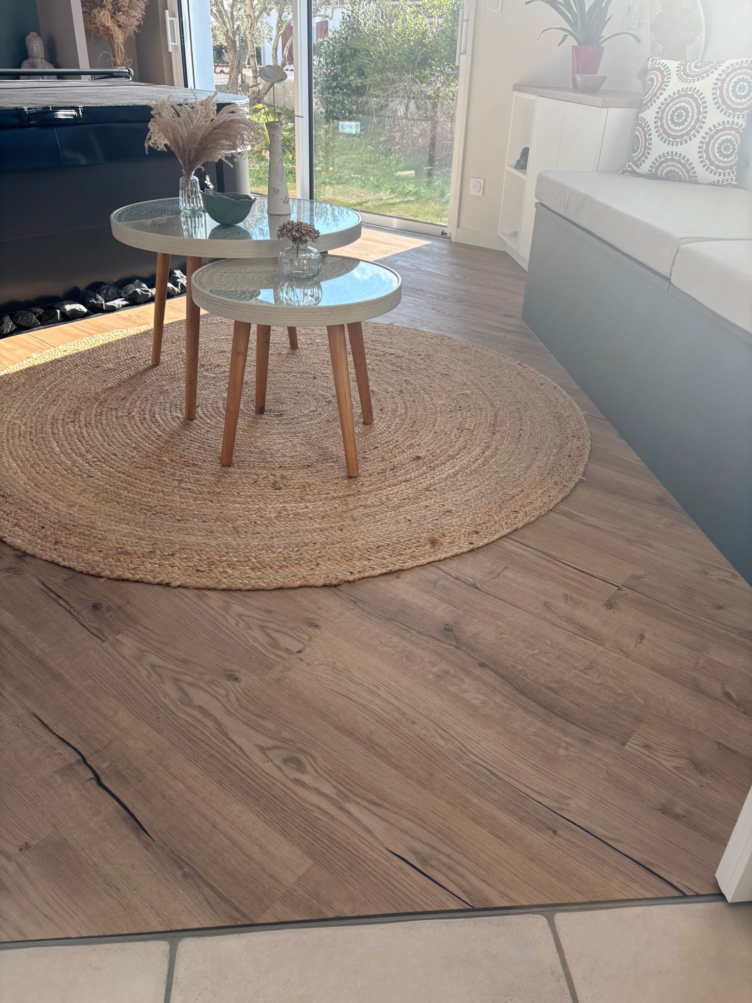 Trois tables rondes avec plateaux en verre, des fleurs et un tapis circulaire en jute sur un sol imitation bois.