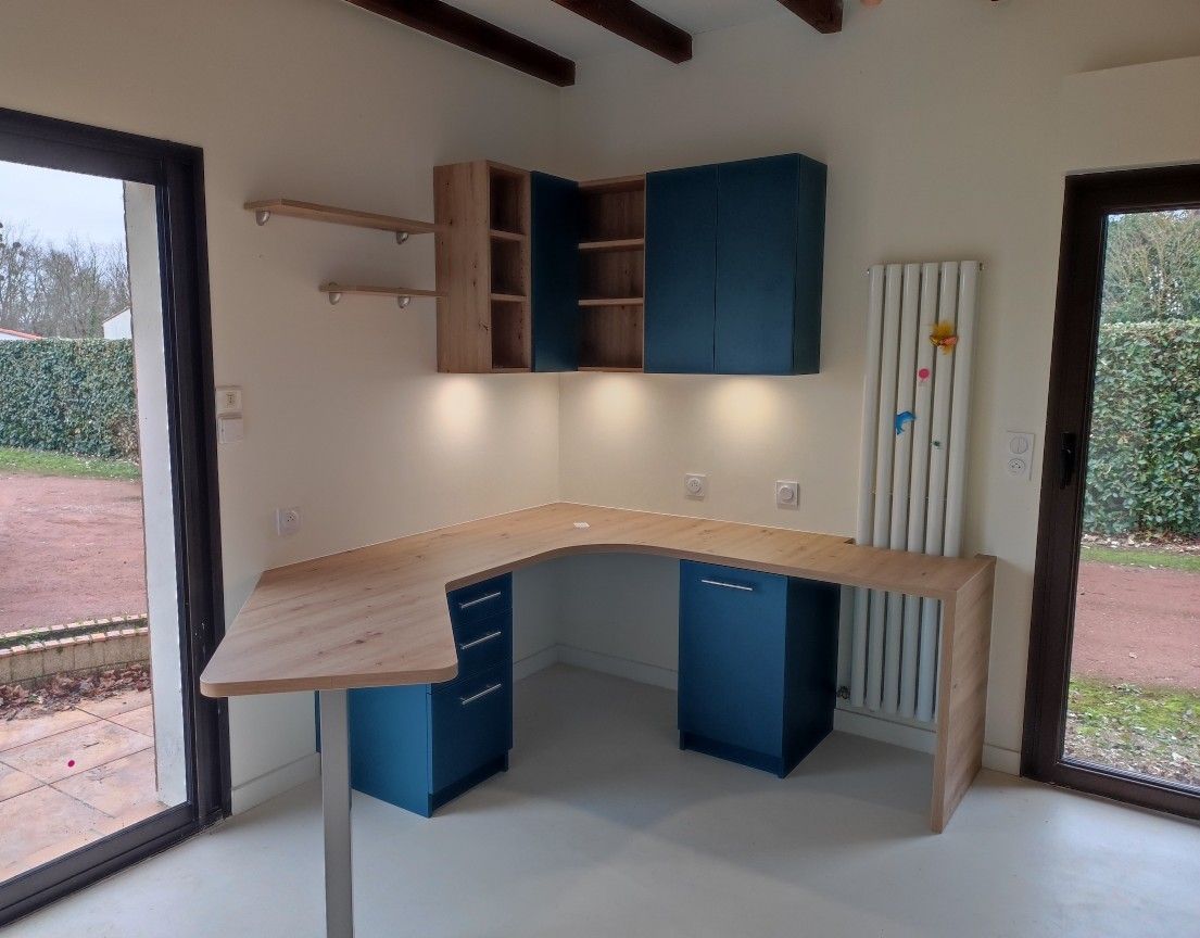 Bureau en L avec armoires bleues et meuble d'angle dans une pièce avec de grandes fenêtres, bois naturel.