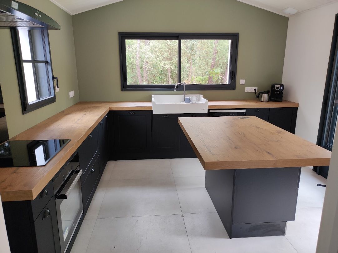 Cuisine moderne avec placards noirs, comptoirs en bois et îlot central. Murs vert olive.